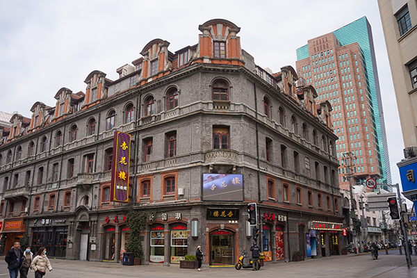 一棟歷史悠久的老建築，位於現代城市中心，外觀有傳統與現代相融合的特色，街道上有行人和商店。