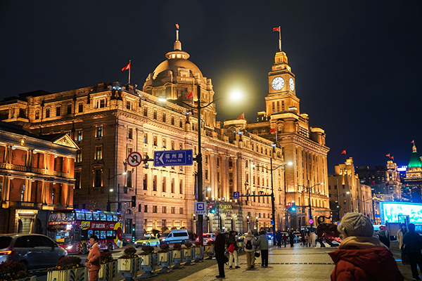 上海外灘的歷史建築在夜間燈光下閃耀，街道上有行人與車輛穿梭。